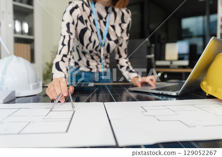 Architect woman working with blueprints for sketching a construction project, green energy and solar panel concept. Architect woman working with blueprints for sketching a construction project, green energy and solar panel concept. 129052267