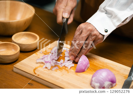 Close up of hands slicing onion on cutting board in kitchen. Close up of hands slicing onion on cutting board in kitchen. 129052276