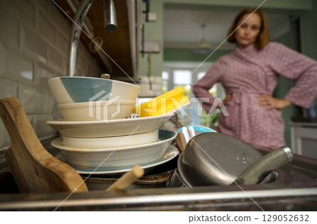 Procrastination, dirty dishes in kitchen, sad woman in the background 129052632