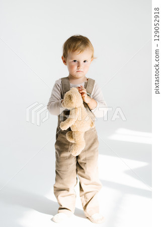 Boy child is holding a stuffed animal, possibly a teddy bear, and appears to be sad 129052918