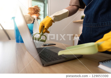 Laptop Cleaning. Person using dustpan to clean keyboard and laptop. 129053300