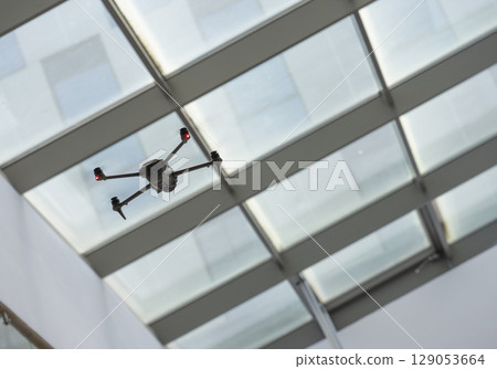 Drone flying indoors under a glass ceiling in a modern building during daylight capturing aerial Drone flying indoors under a glass ceiling in a modern building during daylight capturing aerial 129053664