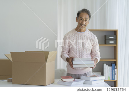 Senior man putting books into cardboard box, looking at camera, moving, decluttering image 129053764