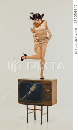 Woman in flapper dress standing shocked on retro TV with exploding champagne image on screen 129054442