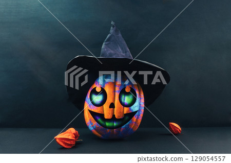 Halloween. A colourful pumpkin in black paper witch's hat and physalis on a dark background. Jack's lantern decorated by childrens. Copy space Halloween. A colourful pumpkin in black paper witch's hat and physalis on a dark background. Jack's lantern decorated by childrens. Copy space 129054557