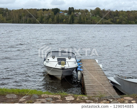 Boat docked at wooden pier by serene lake in early spring Boat docked at wooden pier by serene lake in early spring 129054885