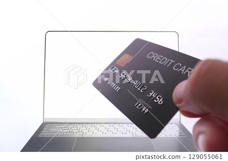 Online payment with credit card held in hand in front of laptop screen, secure digital transaction. 129055061