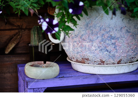 Floral arrangement with a weathered pot and a stone ashtray on a rustic purple table in a garden setting 129055360
