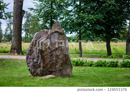 Large natural rock formation stands prominently in a green park surrounded by trees during a cloudy day 129055376