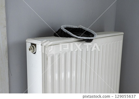 A gray towel is draped over a white radiator, which is positioned against a gray wall. A gray towel is draped over a white radiator, which is positioned against a gray wall. 129055637