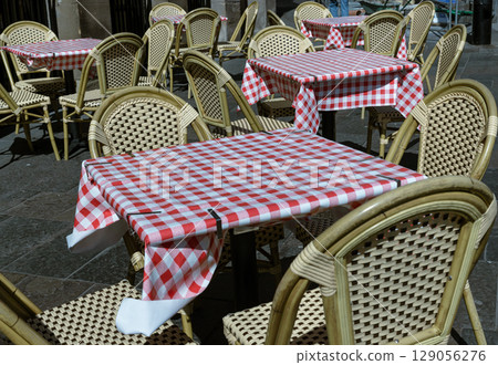 Empty tables and chairs with red and white checkered tablecloths with chairs outside a cafe on street. Empty tables and chairs with red and white checkered tablecloths with chairs outside a cafe on street. 129056276