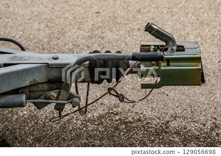 Trailer Hitch Coupling Mechanism On Paved Surface: Close-Up Of Metal Tow Bar With Brake Cable, Rubber Sleeve, And Mounting Hardware For Towing Connection 129056698