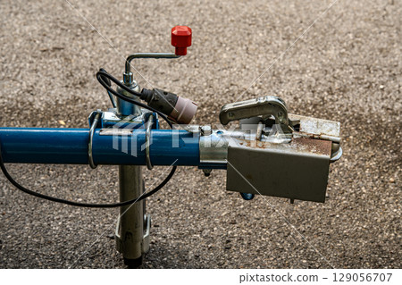Trailer Hitch Coupling Mechanism On Paved Surface: Close-Up Of Metal Tow Bar With Brake Cable, Rubber Sleeve, And Mounting Hardware For Towing Connection 129056707