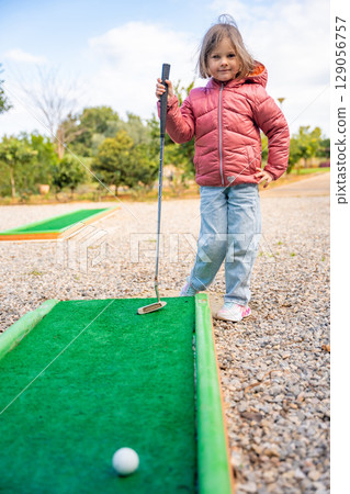 Little girl playing mini golf outdoor. Child having fun with new activity in spring time. Family vacations or resort. 129056757