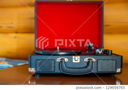 Open vintage record player in suitcase design with vinyl lying nearby. Retro music setup ready for playback in warm, nostalgic atmosphere. Open vintage record player in suitcase design with vinyl lying nearby. Retro music setup ready for playback in warm, nostalgic atmosphere. 129056765