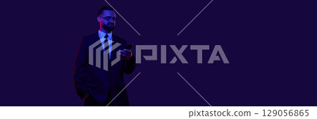 Businessman in dark suit using smartphone against deep blue background. Banner 129056865