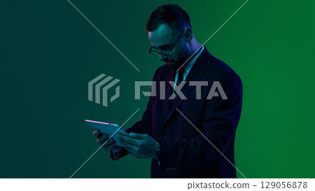 Businessman in suit uses a tablet against a green and blue background. 129056878