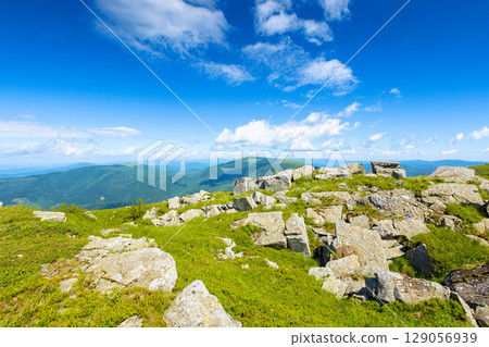wonderful mountain landscape in summer. wide scenery with rock among grass on the hills and slopes under blue sky with fluffy clouds at high noon. scenic view of alpine environment 129056939