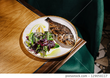 Grilled fish with fresh salad served on a white plate in a cozy restaurant 129058117