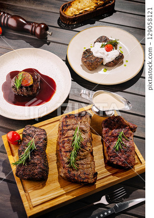 Gourmet steak dishes served on a wooden platter with elegant garnishes Gourmet steak dishes served on a wooden platter with elegant garnishes 129058121