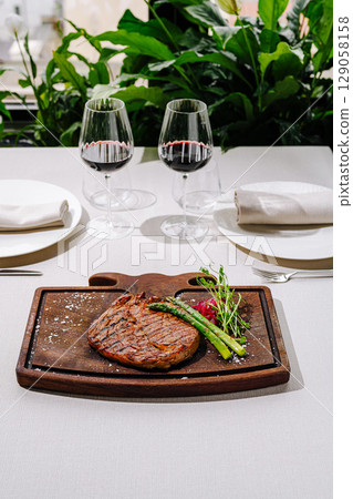 Elegant dining setup featuring steak and wine in a lush environment Elegant dining setup featuring steak and wine in a lush environment 129058158