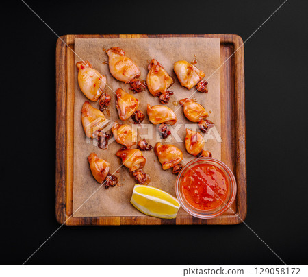 Delicious grilled squid with dipping sauce served on a wooden platter 129058172