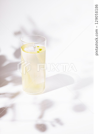 A sleek and modern cocktail served in a tall, clear glass with a single large ice shard and delicate drops of bright yellow oil floating on top 129058186