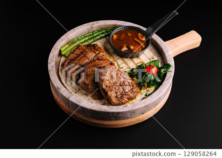Grilled steak served on a sizzling stone with vegetables and sauce Grilled steak served on a sizzling stone with vegetables and sauce 129058264