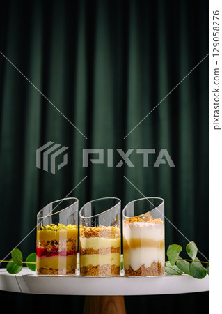 Delicious dessert cups stacked with layers of fruit and cream on a white table Delicious dessert cups stacked with layers of fruit and cream on a white table 129058276