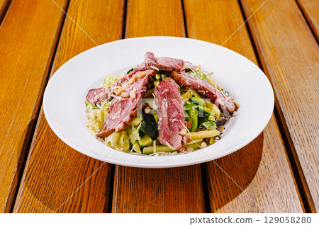 Fresh salad with grilled meat served on a wooden table outdoors 129058280