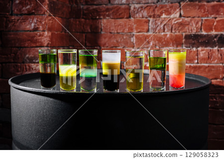 Creative shot glasses lined up on a bar counter with colorful liquids Creative shot glasses lined up on a bar counter with colorful liquids 129058323