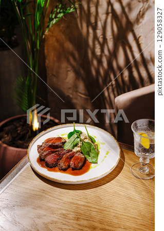 Deliciously plated gourmet dish with greens and drink in elegant setting 129058327