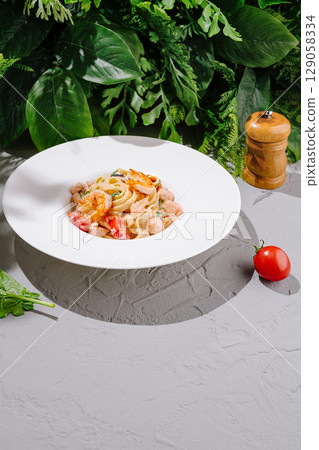 Fresh pasta dish with vegetables served on a white plate in a natural setting 129058334