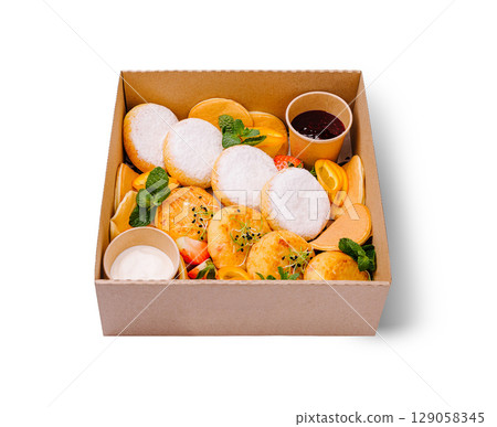 A delightful breakfast box featuring fluffy cottage cheese pancakes dusted with powdered sugar, golden cheese fritters, mini pancakes, fresh fruit slices, and cups of jam and sour cream A delightful breakfast box featuring fluffy cottage cheese pancakes dusted with powdered sugar, golden cheese fritters, mini pancakes, fresh fruit slices, and cups of jam and sour cream 129058345