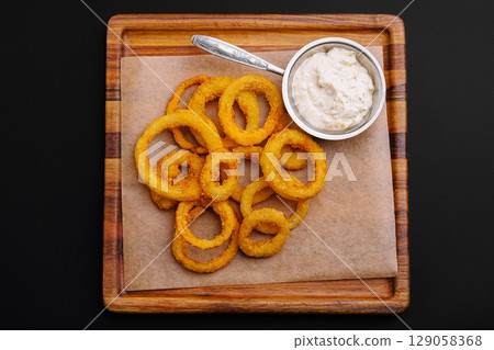 Crispy onion rings served with creamy dipping sauce on a wooden platter 129058368