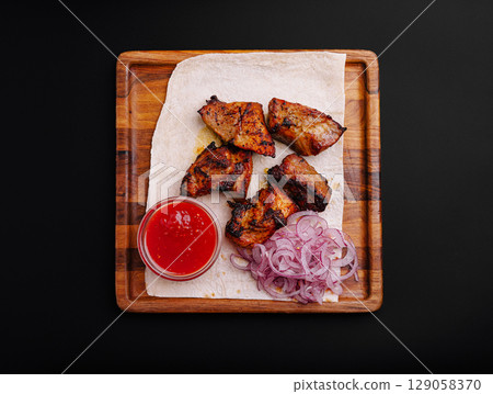Delicious grilled meat served with onions and spicy sauce on a wooden platter Delicious grilled meat served with onions and spicy sauce on a wooden platter 129058370