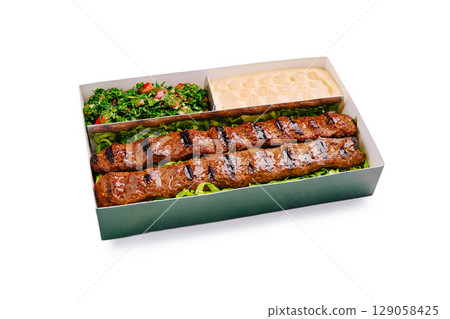 Grilled kebabs served with fresh salad and creamy dip in takeout box 129058425