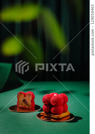 Desserts with vibrant red toppings on a green background under soft lighting Desserts with vibrant red toppings on a green background under soft lighting 129058463