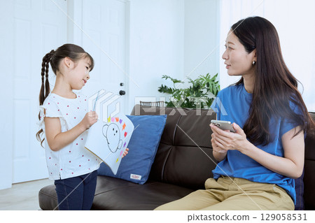 A smiling parent shows a drawing their child has made to their mother A smiling parent shows a drawing their child has made to their mother 129058531