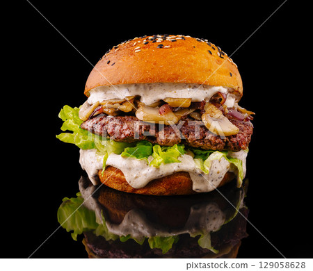 Gourmet burger with lettuce, mushrooms, and creamy sauce on black Gourmet burger with lettuce, mushrooms, and creamy sauce on black 129058628