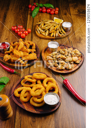 Delicious assortment of fried snacks on wooden plates at a dining table Delicious assortment of fried snacks on wooden plates at a dining table 129058674
