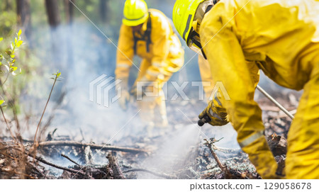 Firefighters combat forest wildfire in protective gear, creating dense smoke 129058678