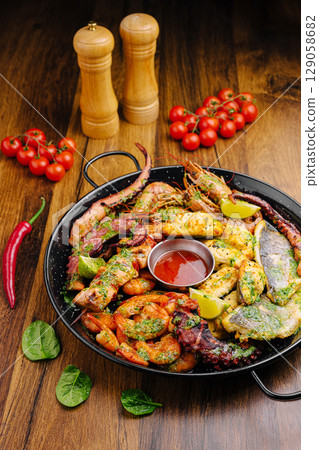 Grilled seafood platter with fresh vegetables and spices on wooden table Grilled seafood platter with fresh vegetables and spices on wooden table 129058682