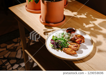 Delicious chicken wings served with fresh salad and rice on wooden table 129058696