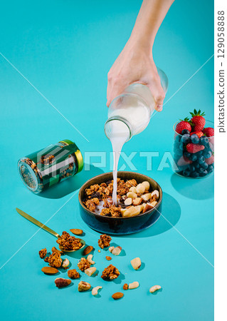 Pouring milk over granola and nuts in a vibrant kitchen setting 129058888