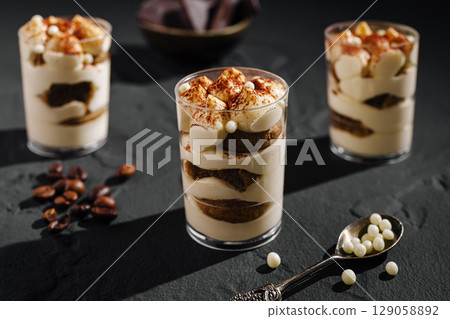 Dessert parfaits with layers of cream, chocolate, and spices on a dark surface Dessert parfaits with layers of cream, chocolate, and spices on a dark surface 129058892