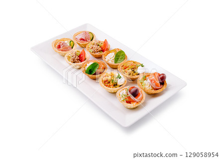Colorful appetizer platter featuring assorted savory tarts on a white plate 129058954
