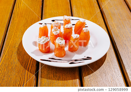 Colorful salmon rolls topped with cream cheese sit artfully on a white plate Colorful salmon rolls topped with cream cheese sit artfully on a white plate 129058999