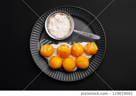 Delicious round snacks served with creamy dip on a stylish black plate 129059001
