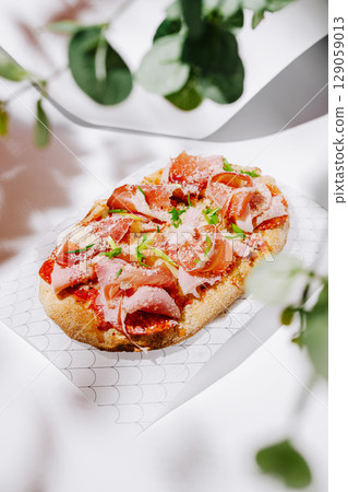 Delicious flatbread topped with meats and herbs presented on a light background Delicious flatbread topped with meats and herbs presented on a light background 129059013